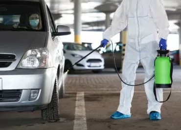 unrecognizable person disinfecting car with spray with woman inside